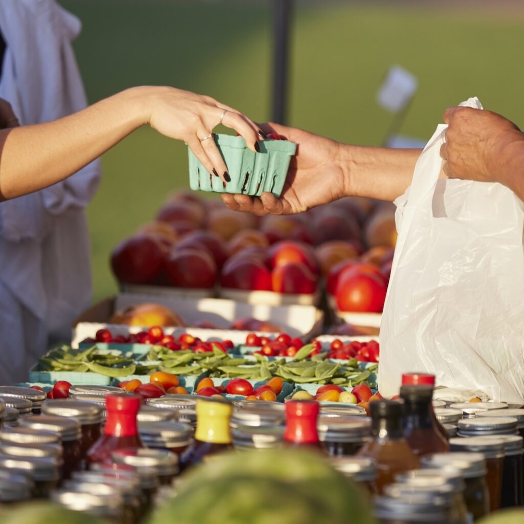 Farmer at market hands purchase to customer over colorful blend of organic produce