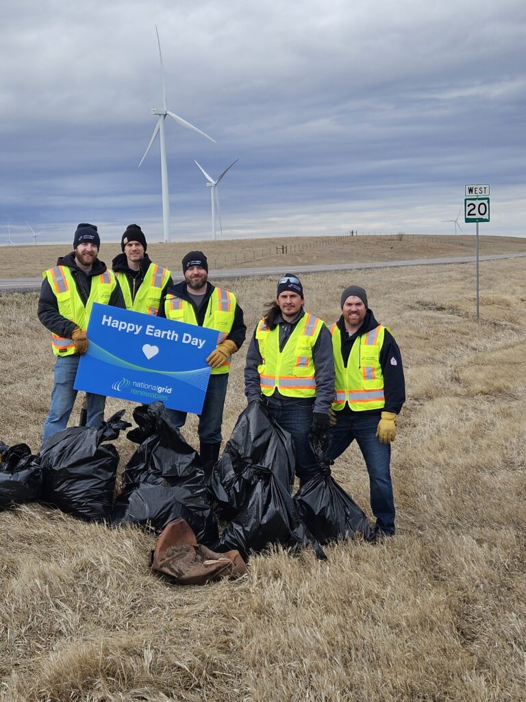 People with Happy Earth Day sign on the side of road by wind turbines